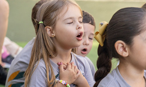 Crianças de olhos fechados com as mãos juntas ao peito em escola cristã bilíngue